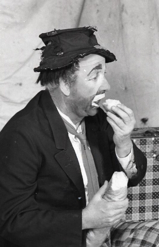 Portrait of a man dressed as a clown eating French bread